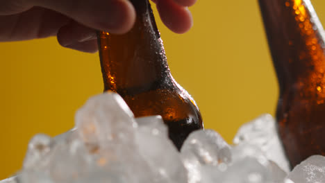 Cerca-De-Una-Persona-Tomando-Una-Botella-De-Vidrio-Fría-De-Cerveza-Fría-O-Refrescos-De-Un-Cubo-Lleno-De-Hielo-Contra-Un-Fondo-Amarillo